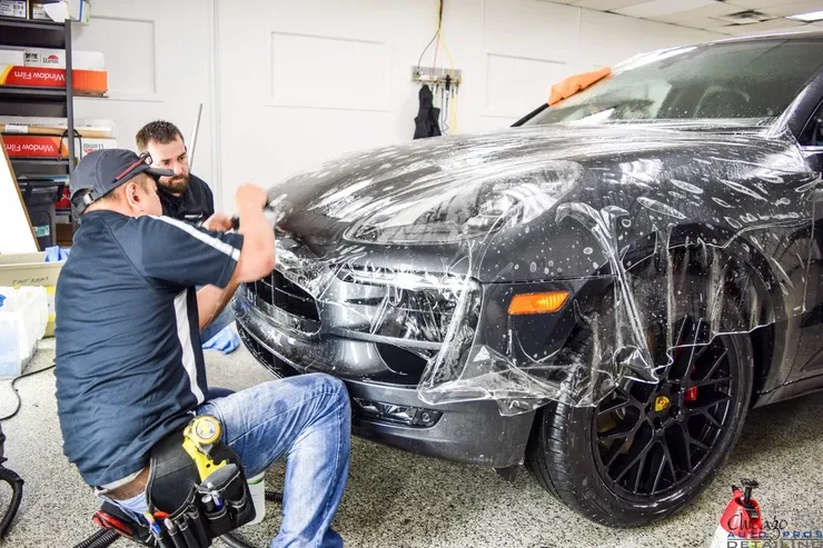 Two men are wrapping a car with plastic wrap in a garage.