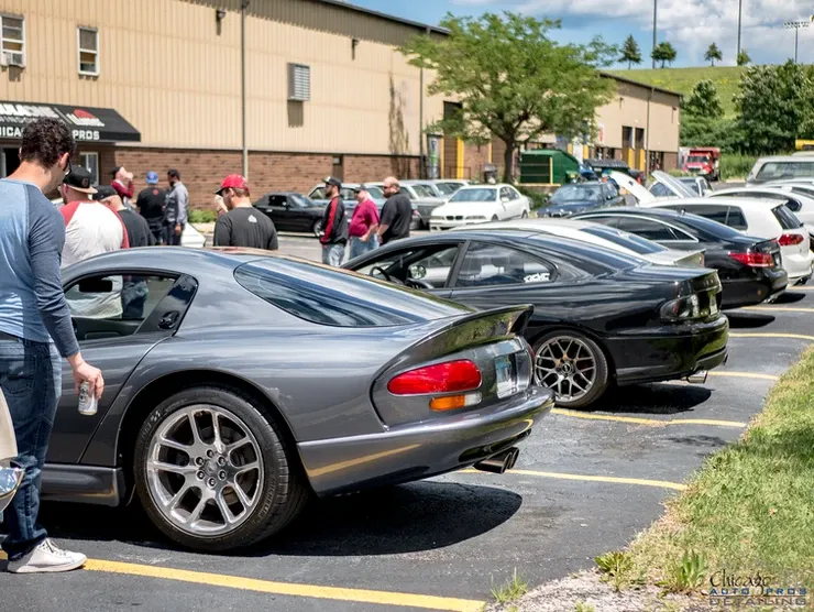 A group of people are standing around a row of cars parked in a parking lot.