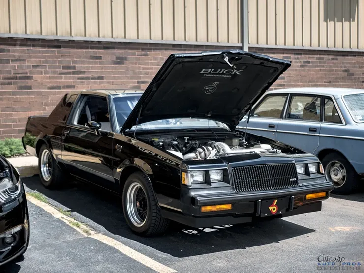 A black car with the hood up is parked in a parking lot.
