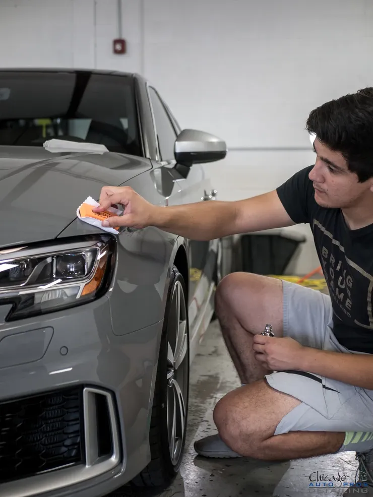 A man is kneeling down next to a car and cleaning it with a cloth.
