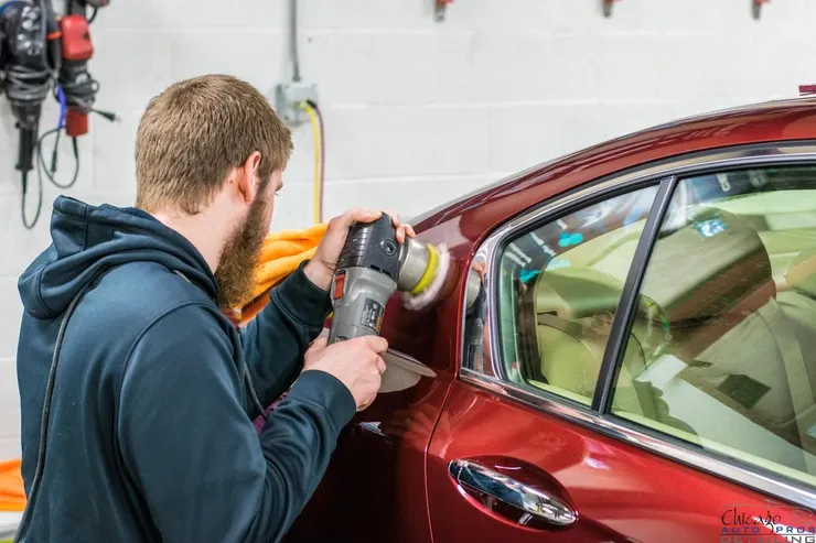 A man is polishing a red car with a machine in a garage.