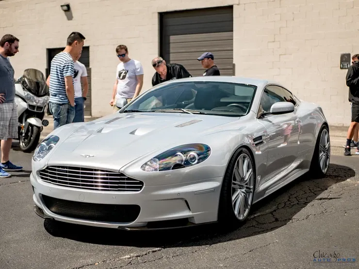 A group of men are standing around a silver sports car.