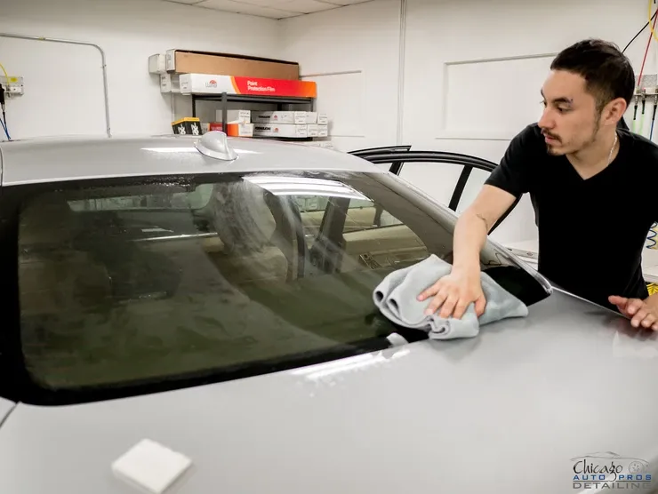 A man is cleaning the windshield of a car in a garage.