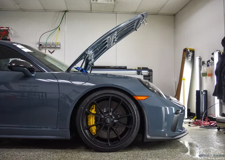 A gray sports car with the hood up in a garage.