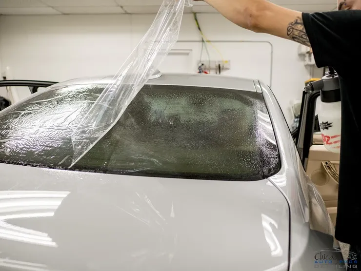 A man is wrapping a white car with plastic.