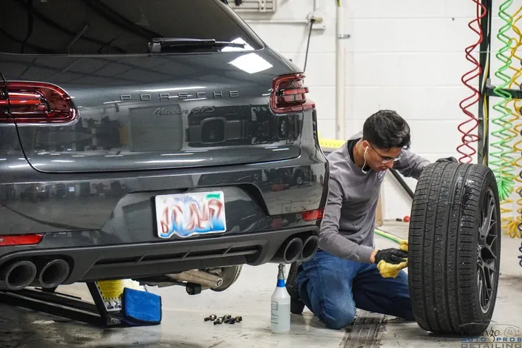 A man is changing a tire on a porsche in a garage.