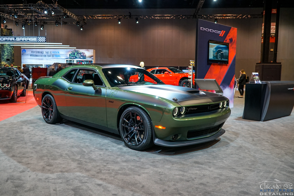 A green dodge challenger is on display at a car show.