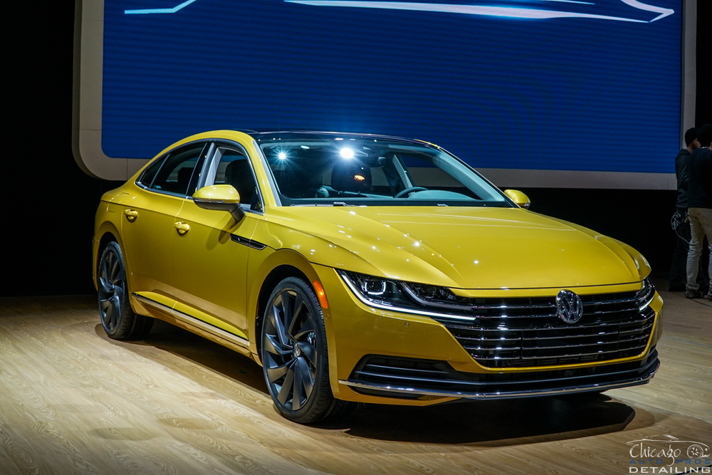 A yellow volkswagen arteon is on display at a car show.