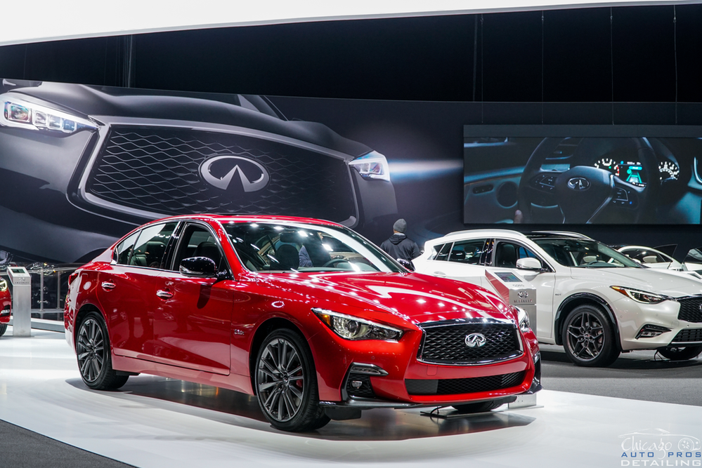 A red infiniti q50 is on display at a car show.