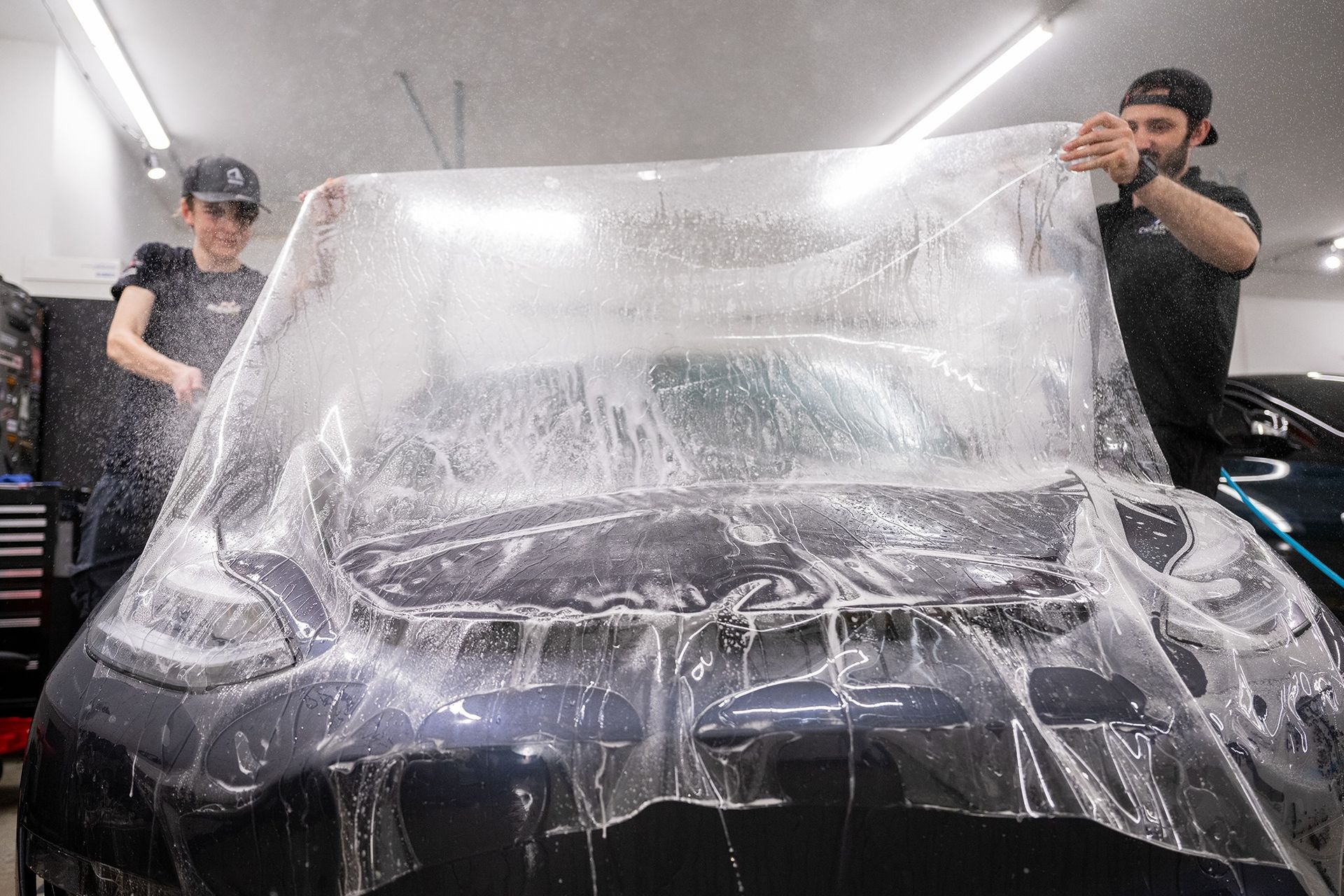 A man and a woman are wrapping a car in plastic.