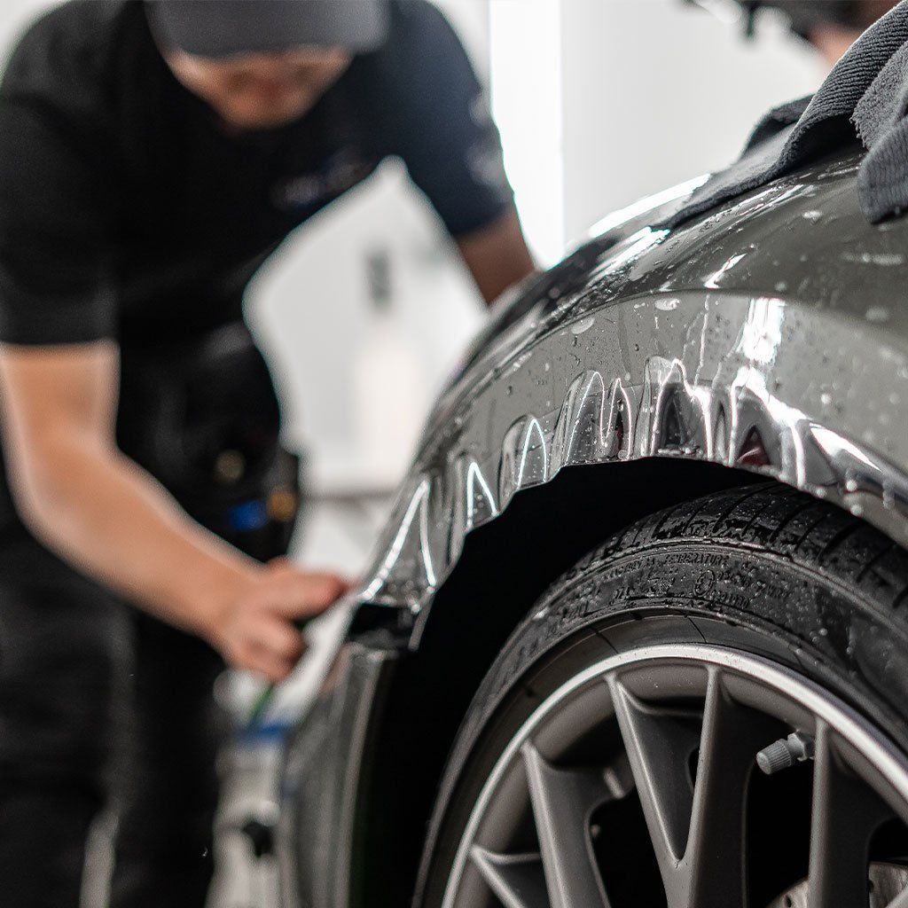 A man is applying a protective film to the fender of a car.