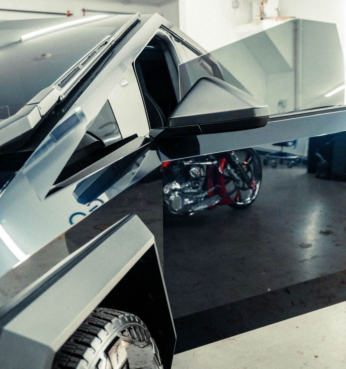 A Cybertruck is parked in a garage next to a motorcycle