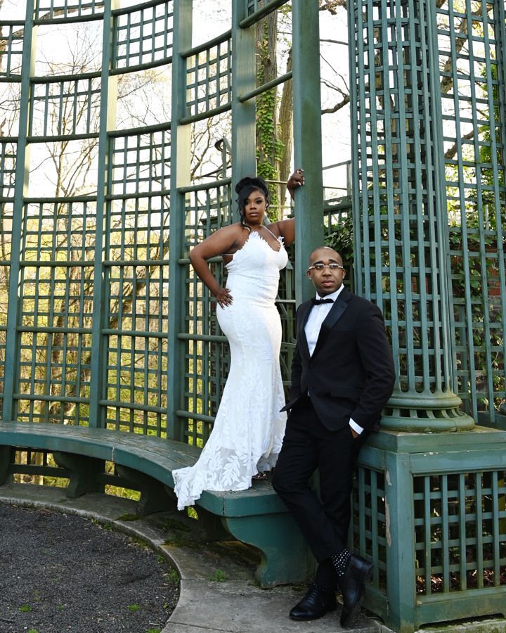 A bride and groom pose for a picture in front of a trellis