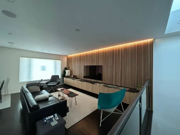 Modern living room with dark wood floors, black leather sofa, teal chair, and neutral curtains.