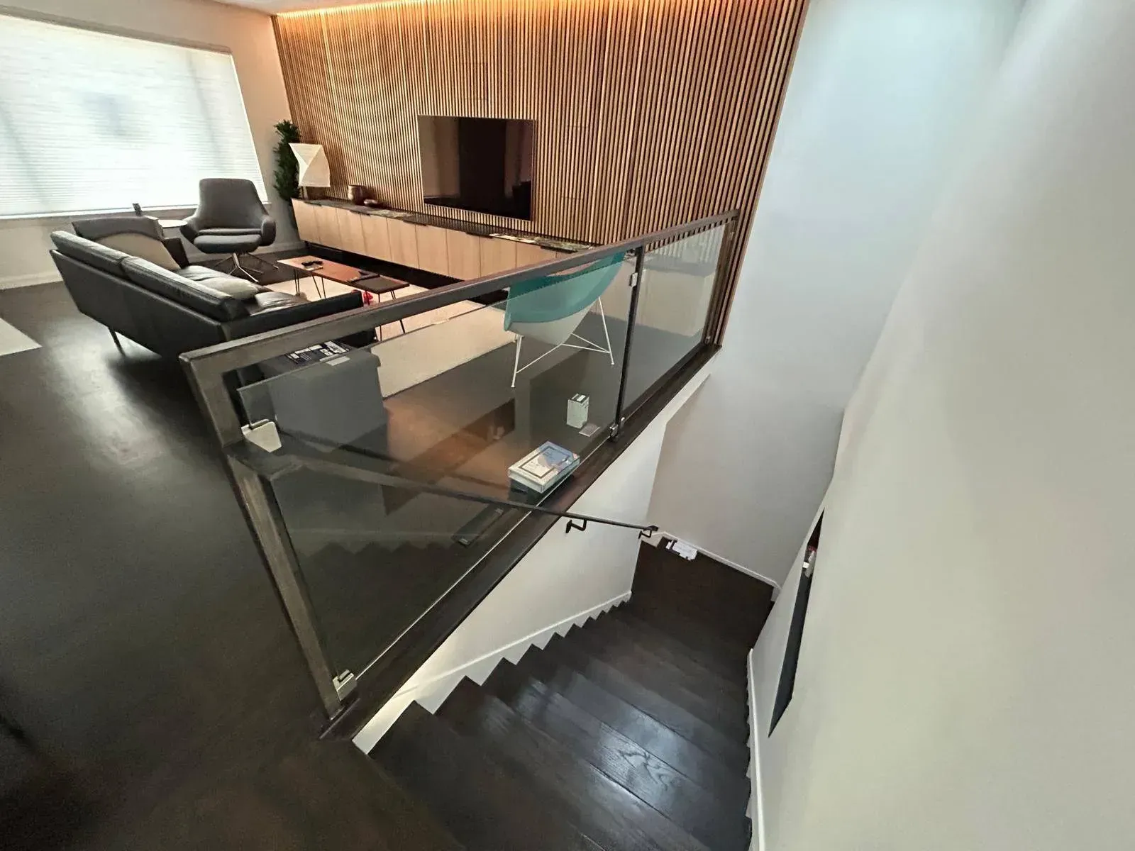 Living room with dark wood floors, glass railing, and a staircase.