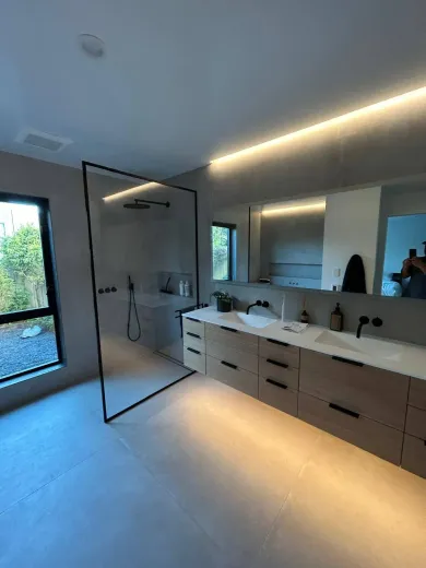 Modern bathroom with glass shower, double vanity, and ambient lighting.