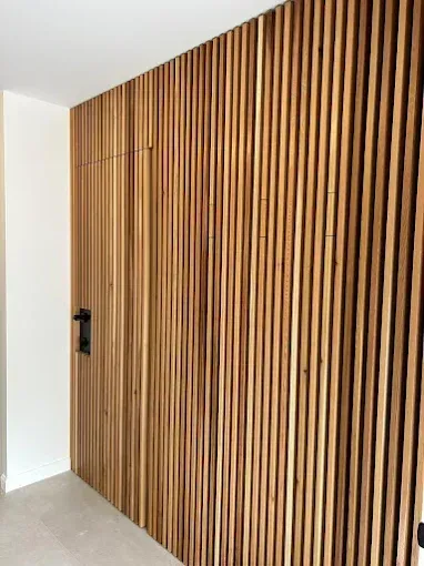 Wood-slat wall and door. The door has a black handle, creating a modern, minimalist interior design.