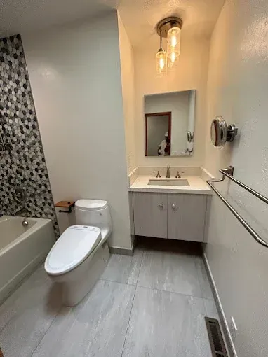 Modern bathroom with gray tile, white vanity, toilet, and shower with mosaic tile.