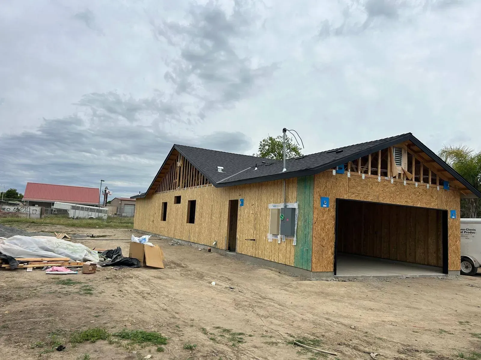 A house under construction with a garage, brown siding, and a black roof against a cloudy sky.