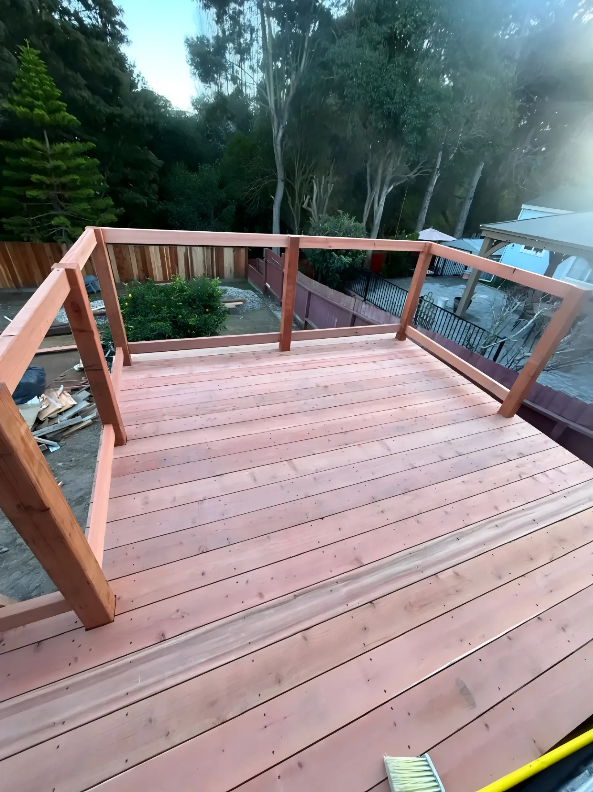 Newly constructed wooden deck with railing, set in a backyard with trees and a fence.