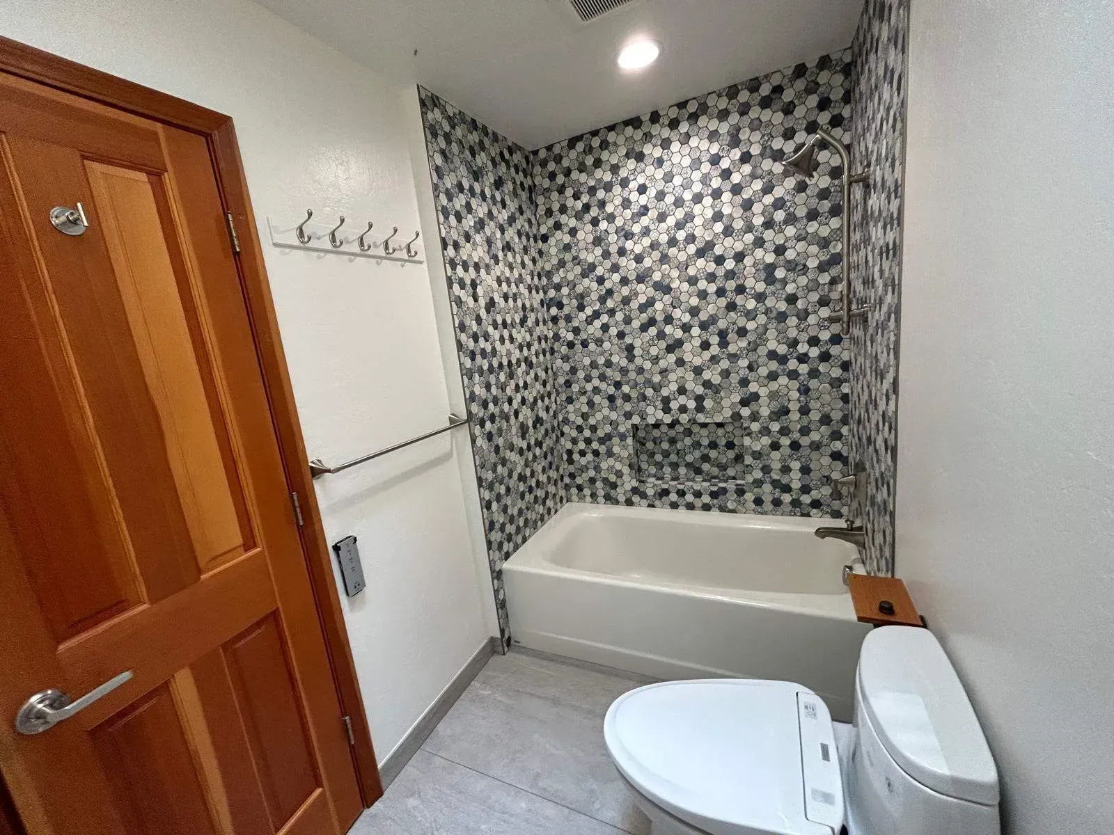 Bathroom with a tiled shower, tub, and a toilet next to it. Brown wooden door on the left.