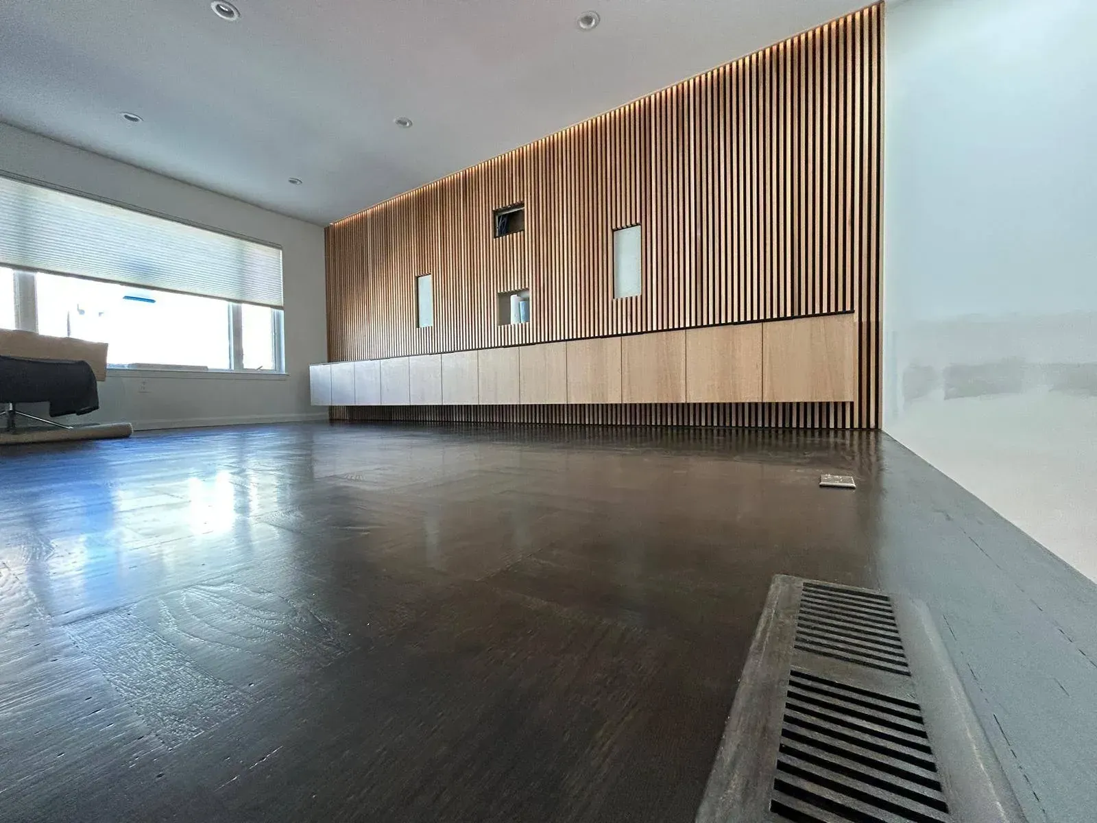 Empty, modern room with wood cabinets, gold curtains, and a shiny dark floor.