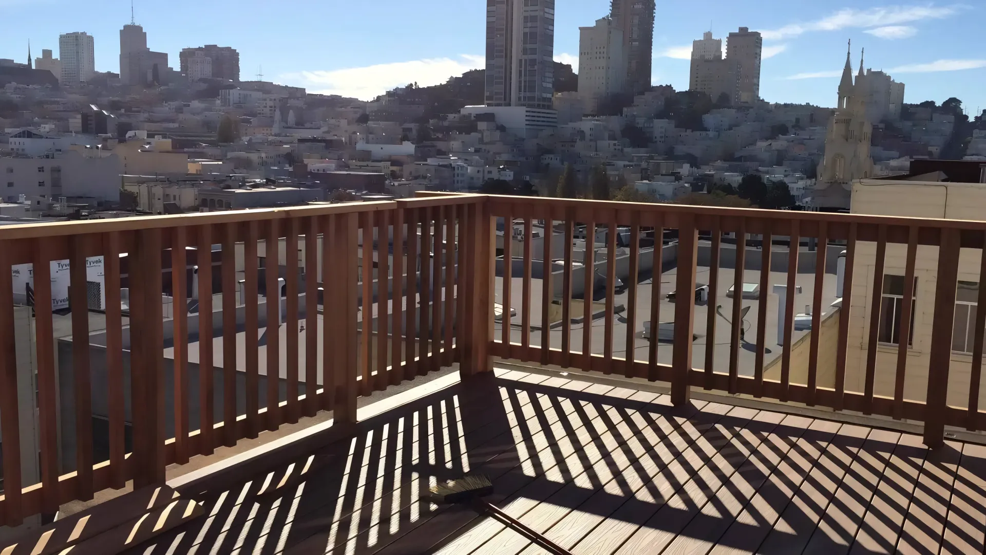 Wooden deck overlooking a city with tall buildings on a sunny day.