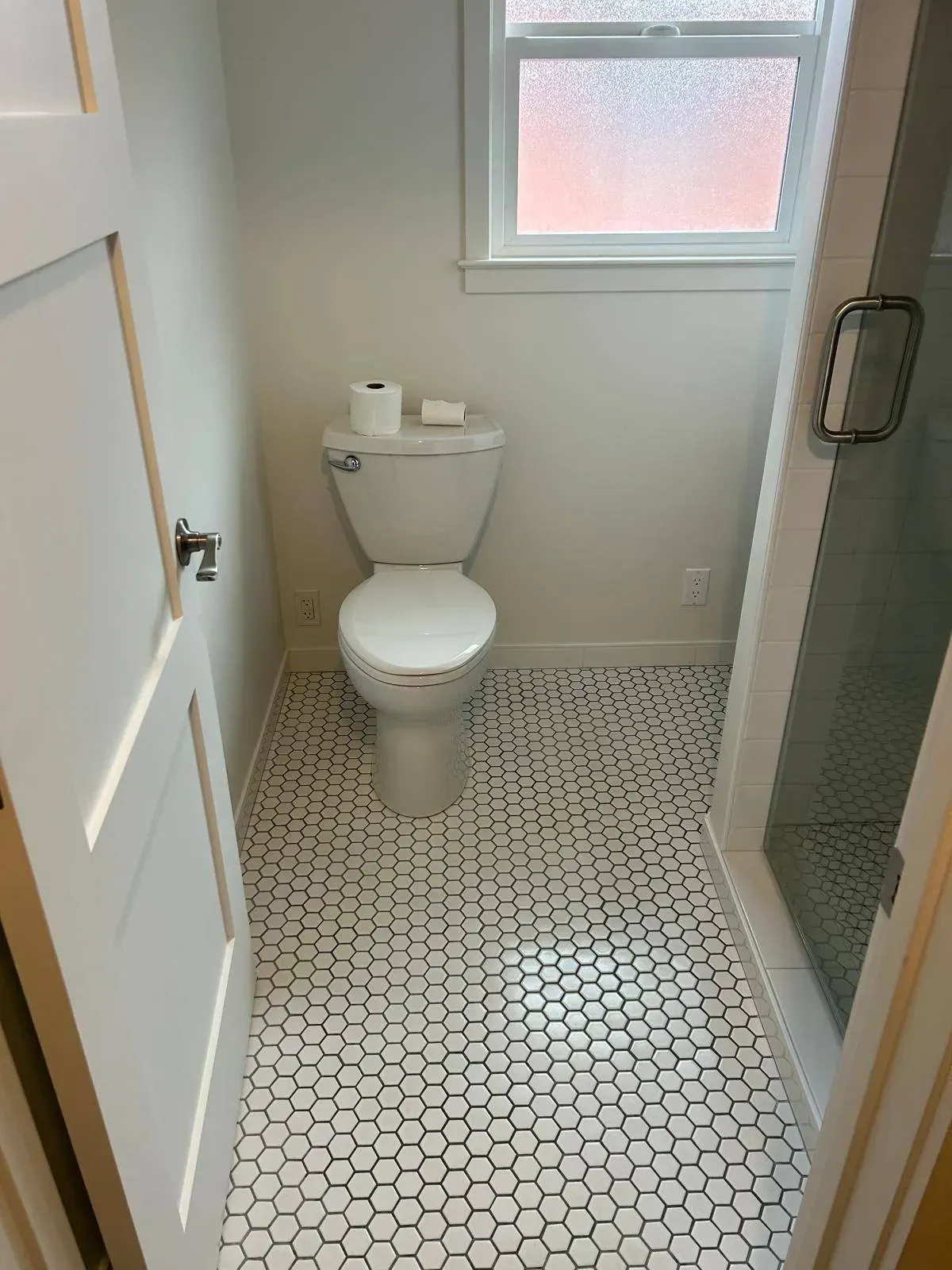 Small bathroom with white toilet, black and white hexagon tile floor, and shower.