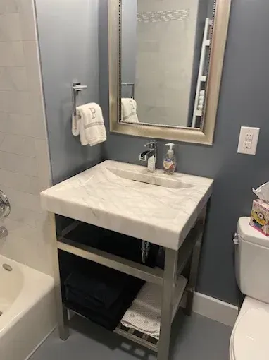 Bathroom with marble sink on silver stand, mirror, towels, blue wall, and toilet.