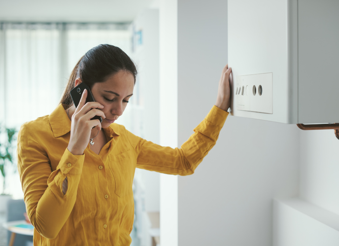 Woman leaning on broken-down boiler in frustration as she waits on the phone