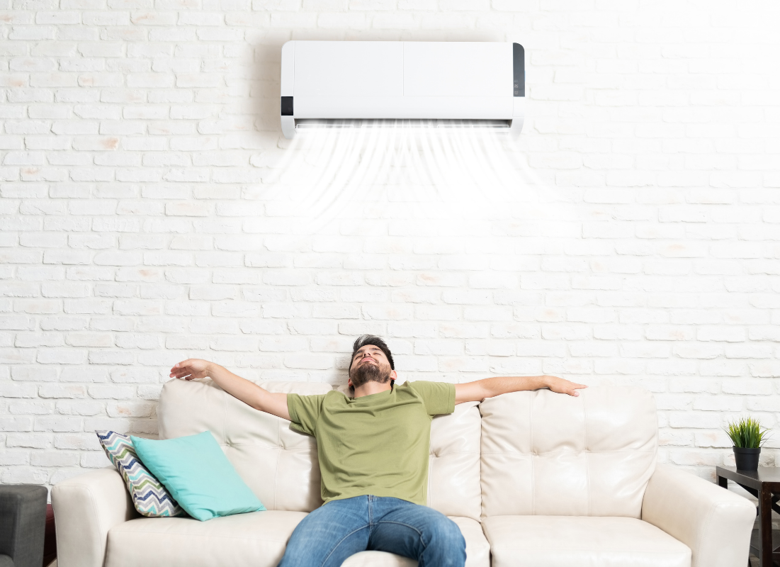 Man relaxing on couch with arms outstretched underneath a mini-split air conditioner on wall in Denver, CO.