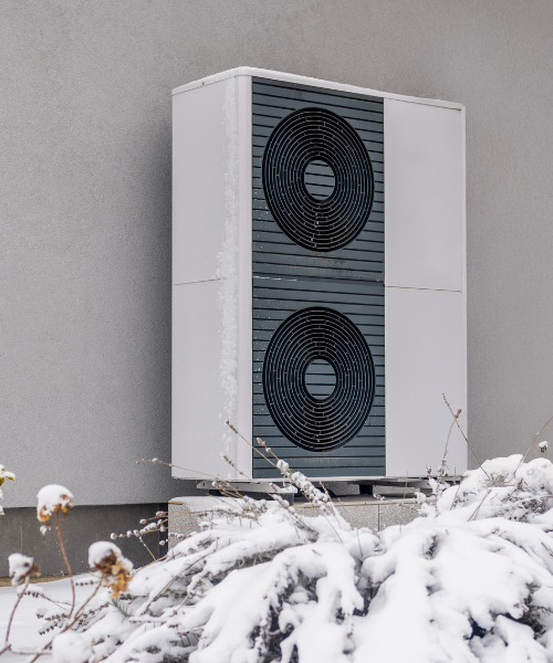 modern double unit heat pump in winter with snow on the ground outside a stucco home in Aurora, CO