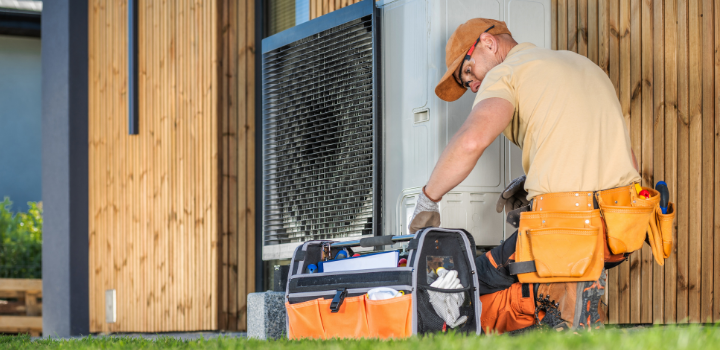 A technician with a tool box working on installing a modern heat pump outside a Denver, CO home