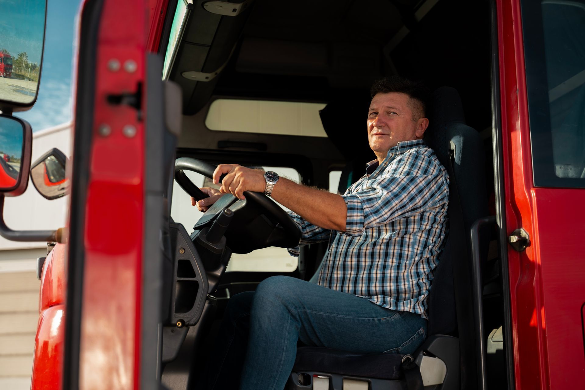 Truck driver smiling while sitting in the cab of a red truck, holding the steering wheel.