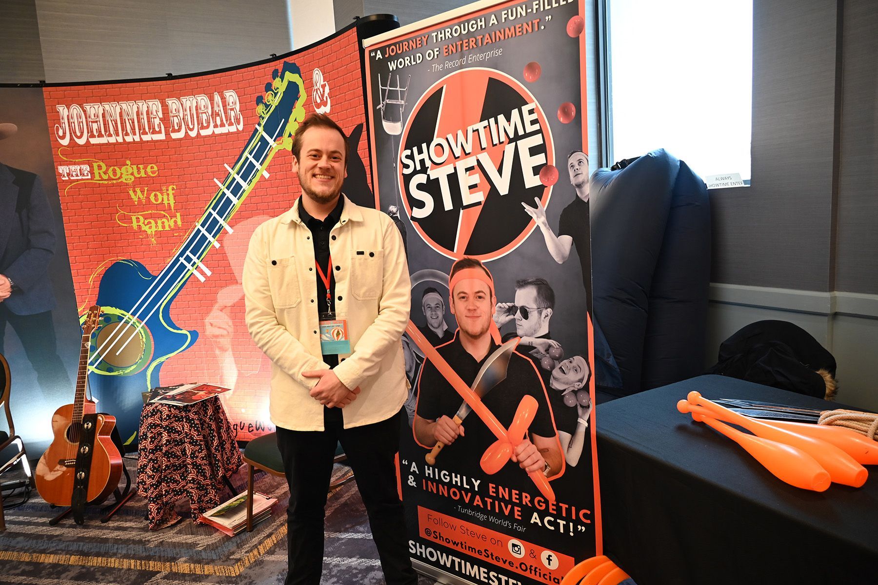 A person smiles while standing between two trade show banners, one for 'Johnnie Bugar' and one for "Showtime Steve.'