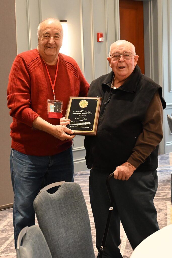 Two people standing in a room, one handing a plaque to the other.