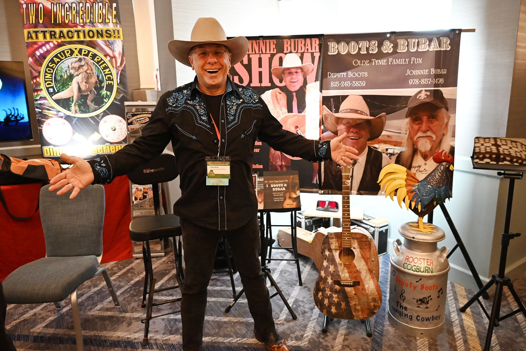 A performer wearing a cowboy hat and western-style shirt stands with arms open before a stage banner and guitar.