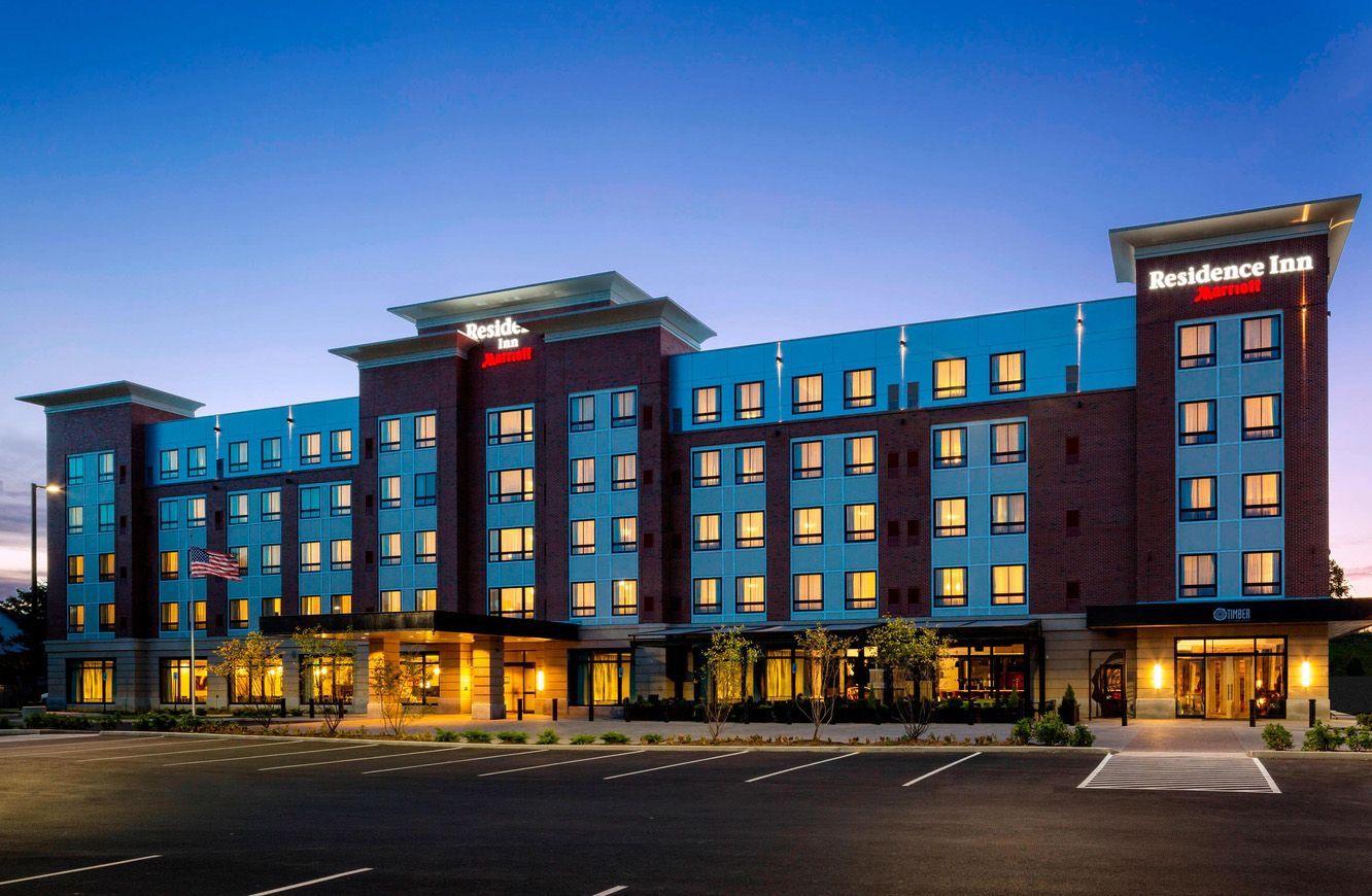 A modern, multi-story Residence Inn by Marriott hotel at dusk, featuring brick accents, light blue panels, and parking.