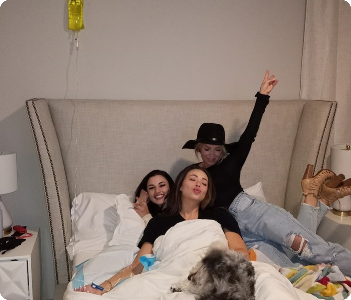 Three women are laying on a bed with a dog