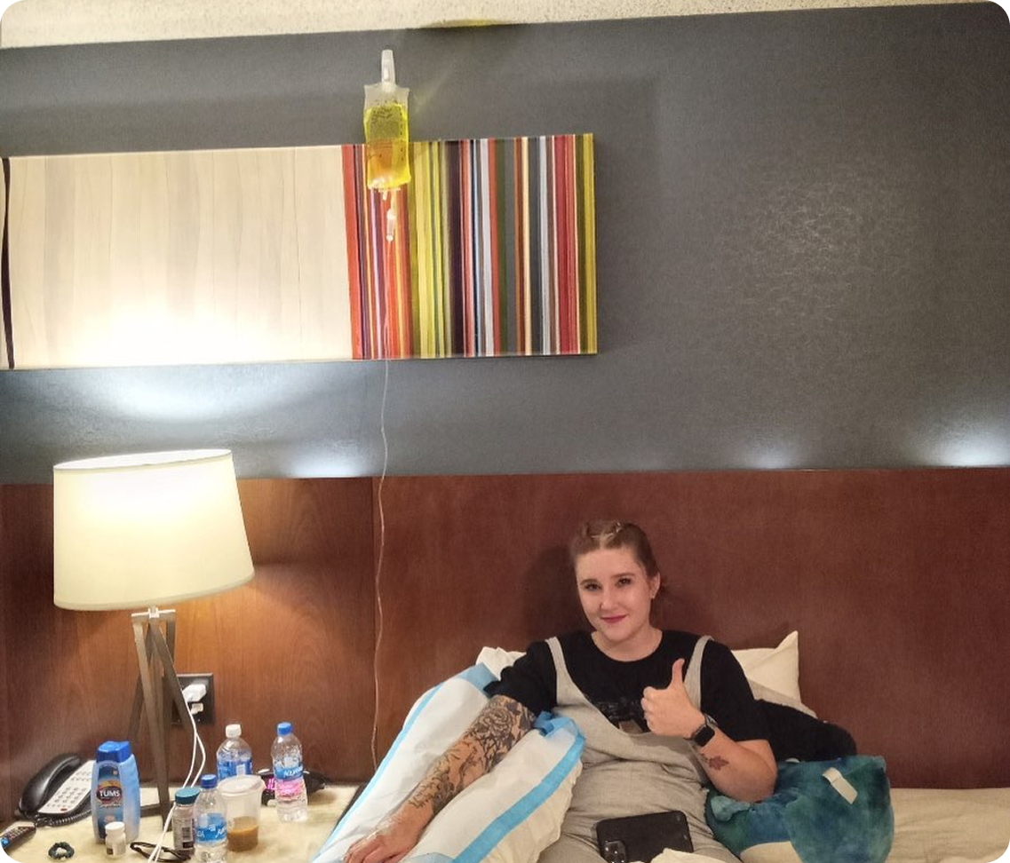 A woman is sitting on a bed giving a thumbs up