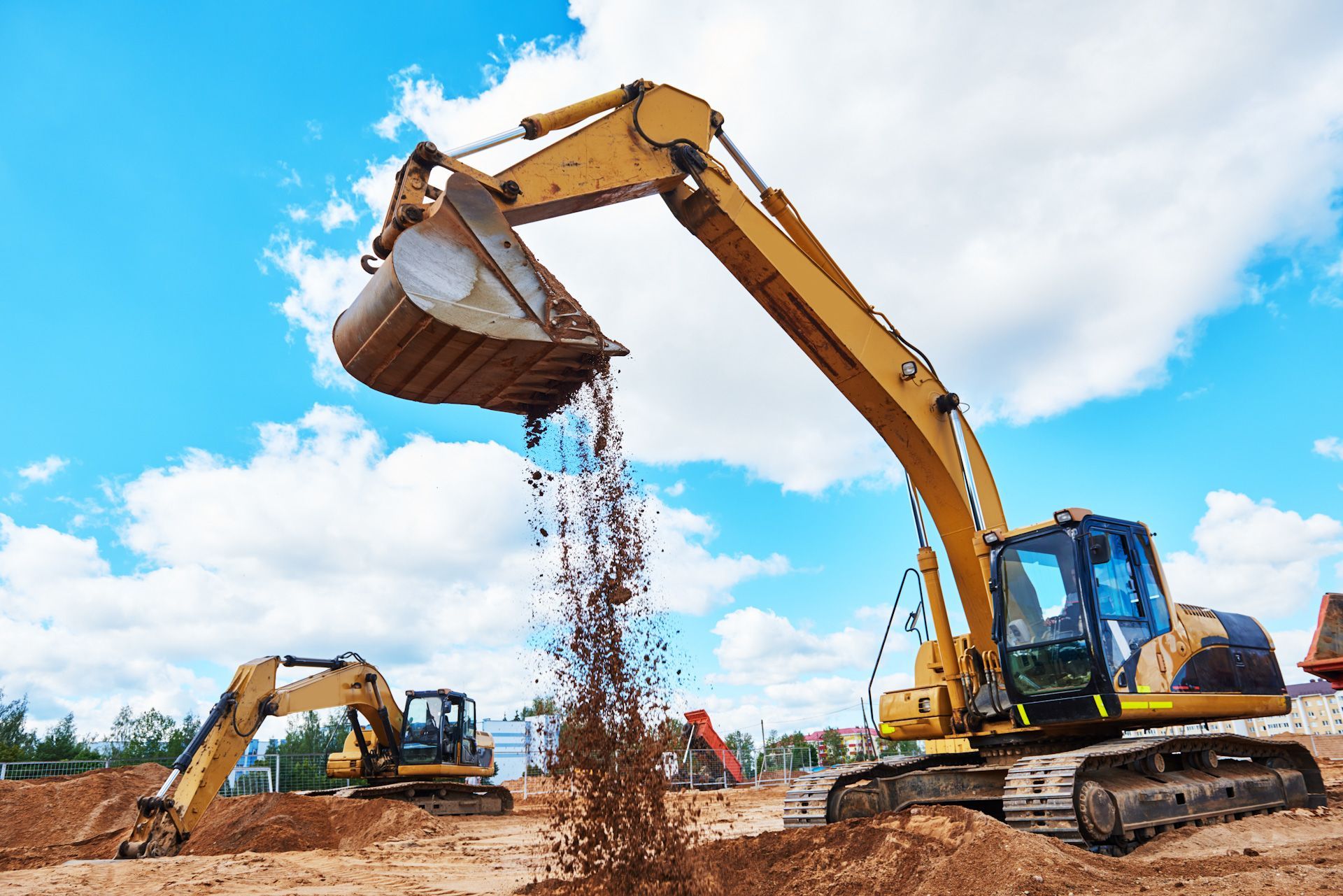 A yellow excavator is pouring dirt from its bucket