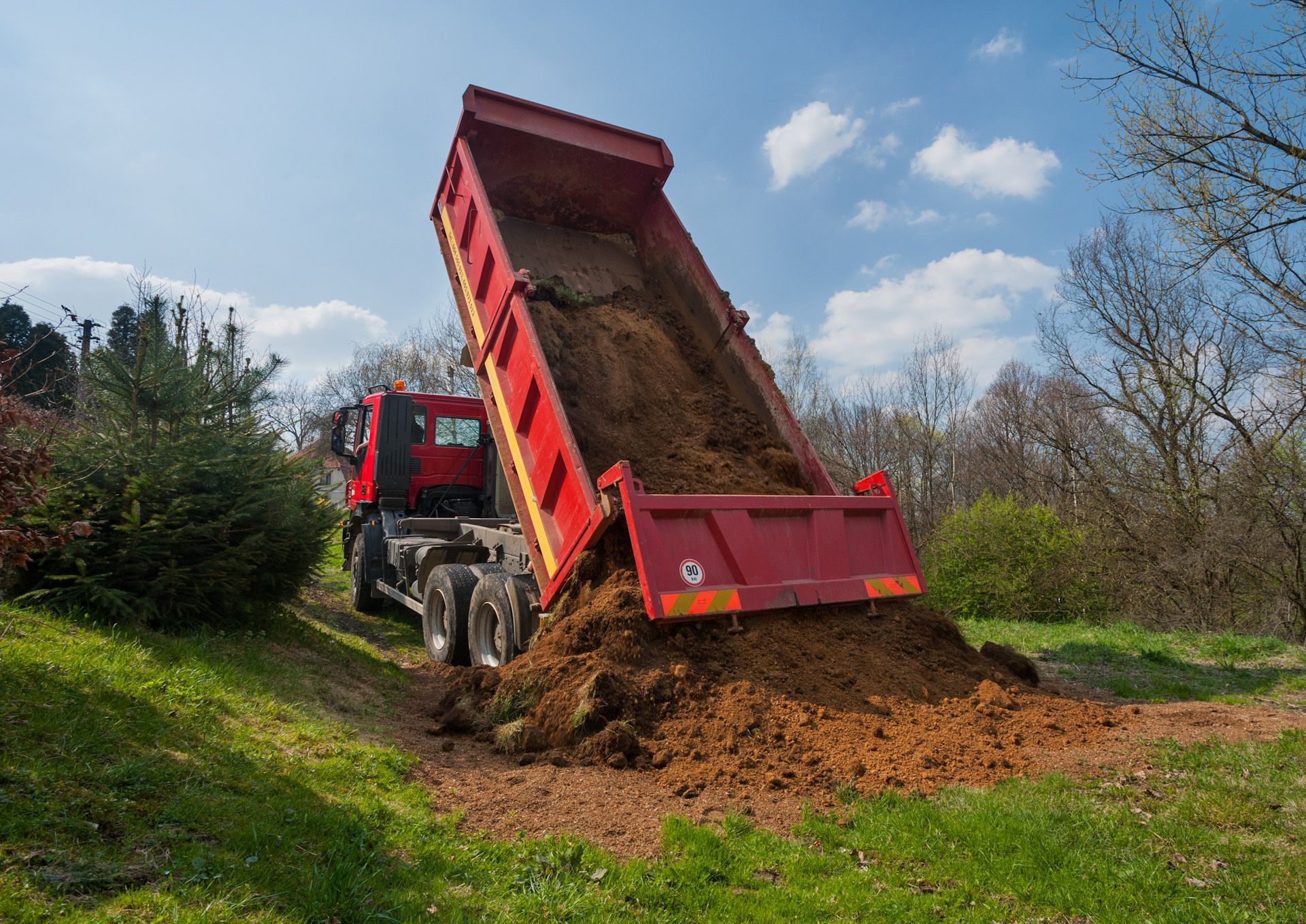 A red dump truck is dumping dirt on a grassy hillside