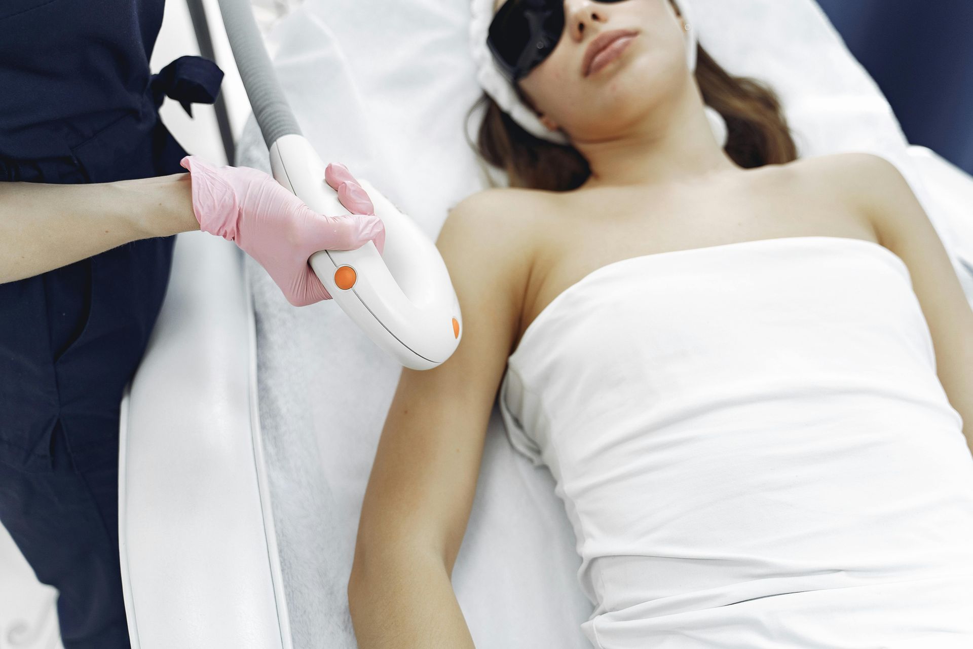 Woman receiving laser hair removal treatment on her arm in a clinic; someone holds the laser device.