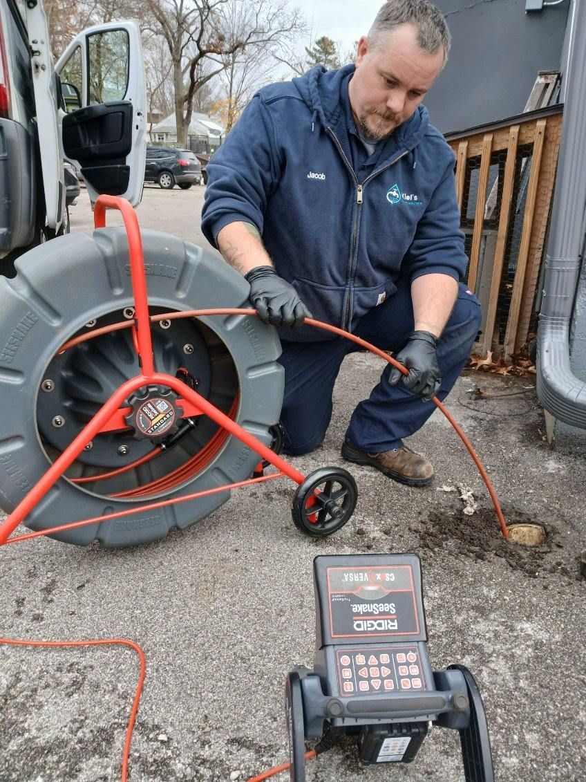 Rusty hose reel with a green hose extending onto a concrete surface. A building and fence are visible in the background.
