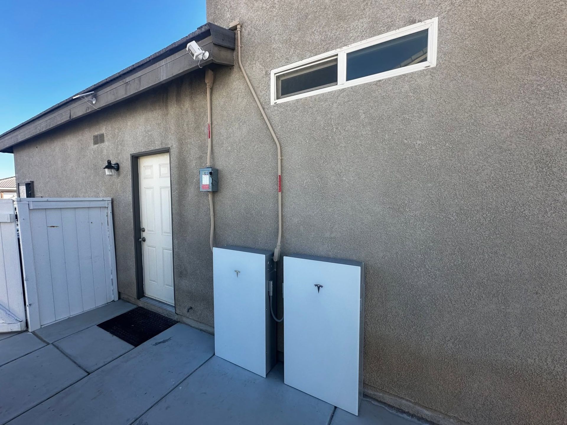 Solar panel and battery storage unit mounted on an exterior wall with electrical wiring.