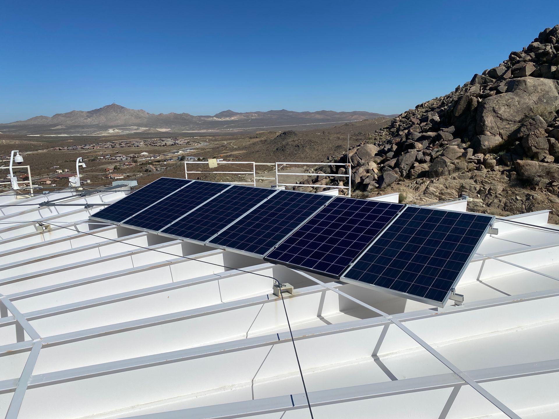 Solar panels mounted on a white rooftop with mountains and desert in the background