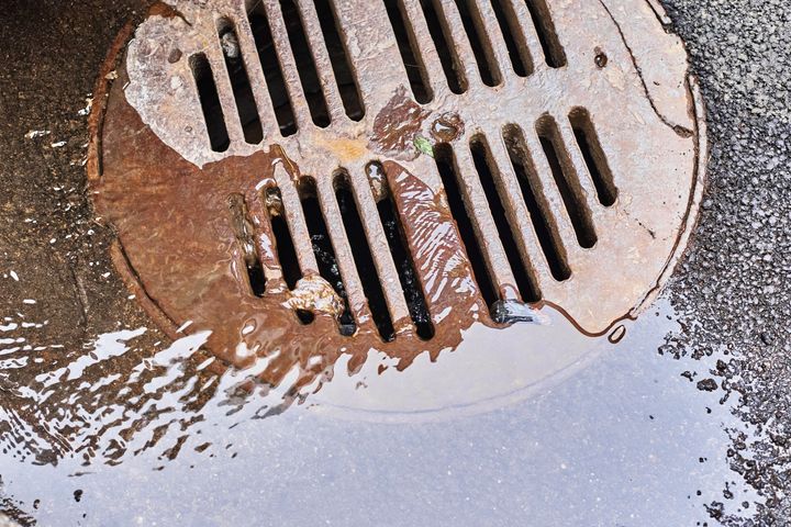 Rusty drain cover with water flowing onto asphalt.