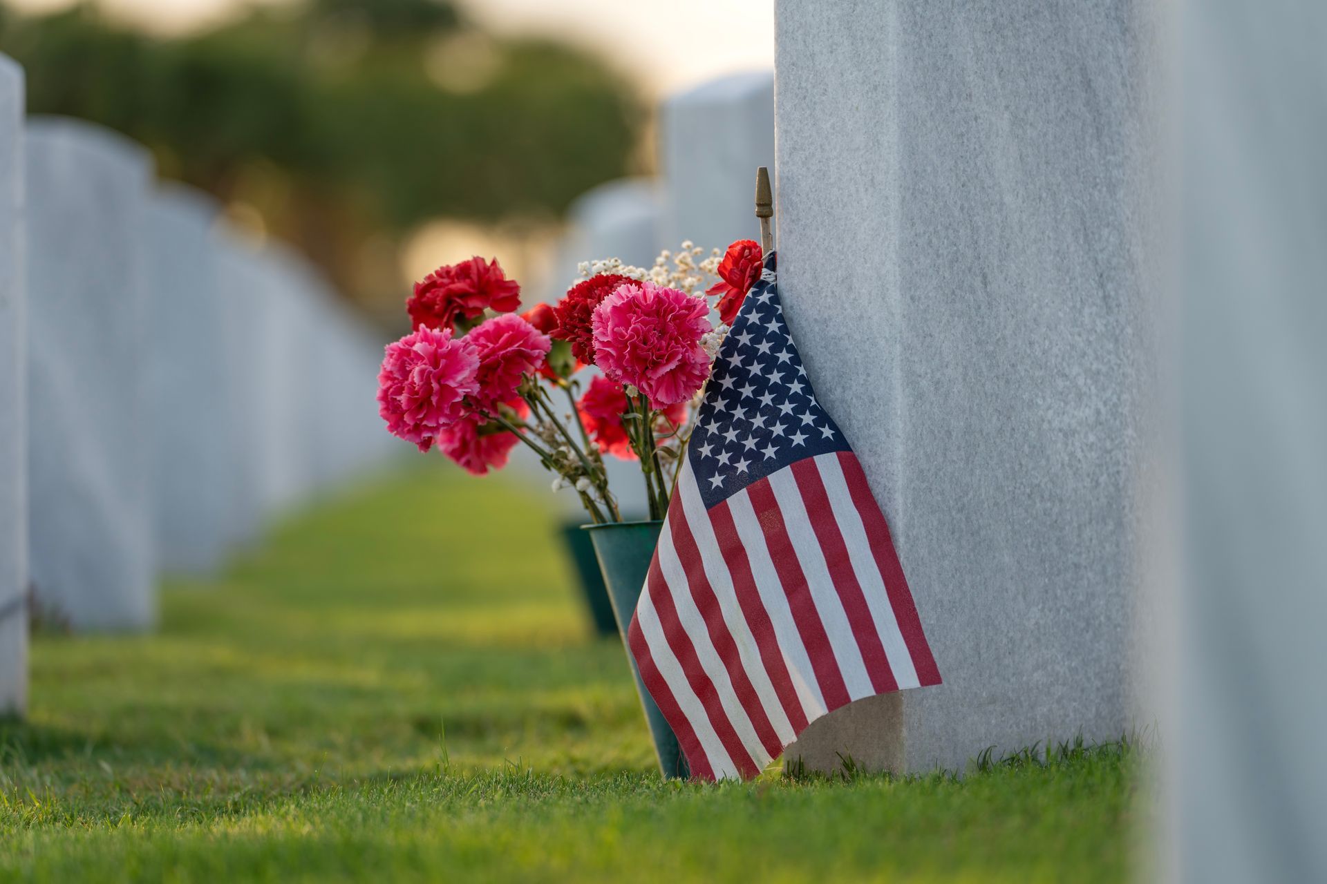 American flag and red flowers placed beside a white headstone in a military cemetery.