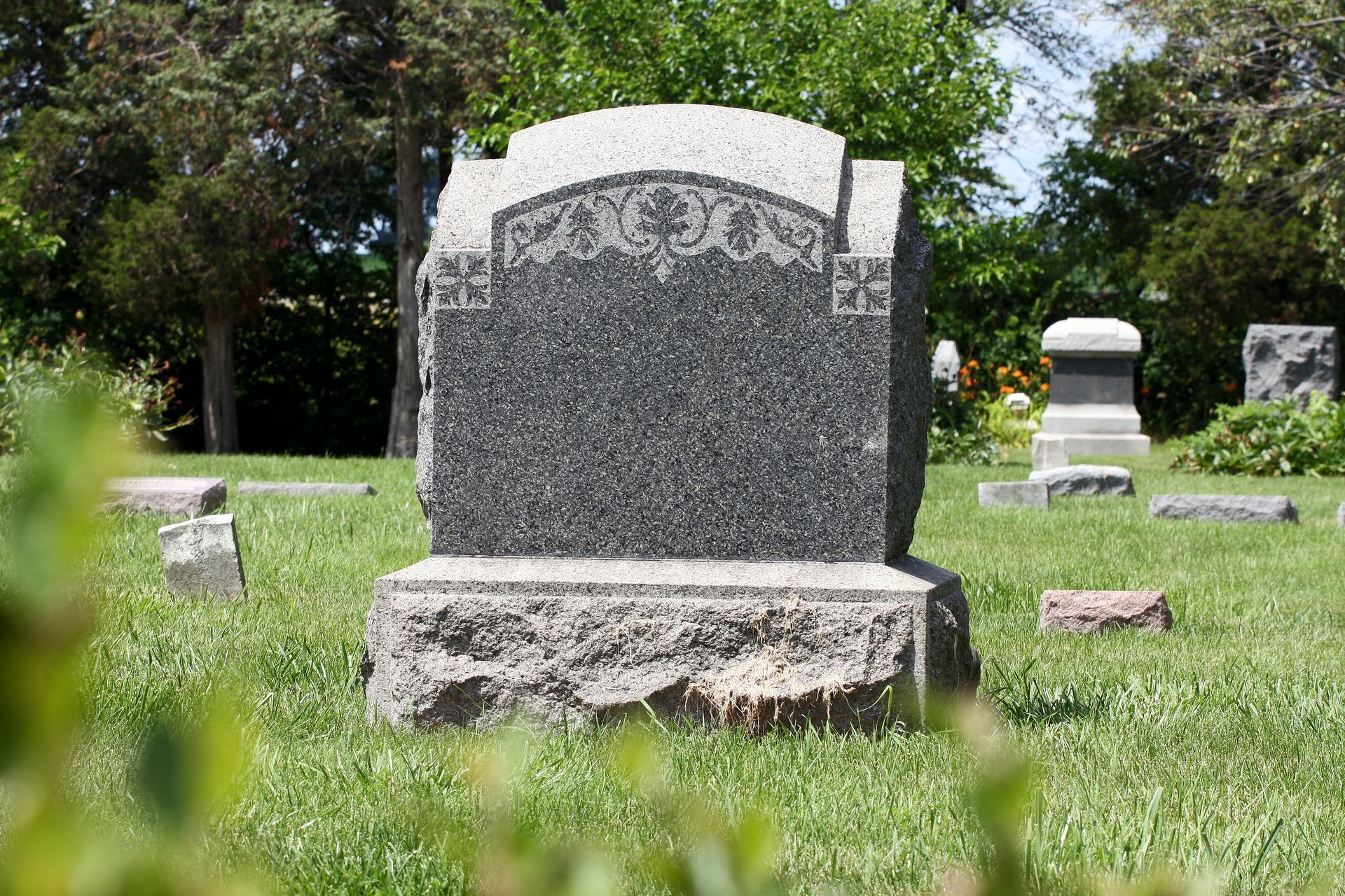 Blank granite upright grave monument with floral engraving on a stone base.