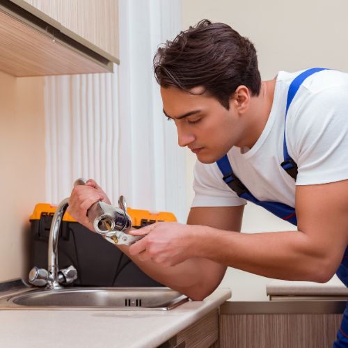 A man is fixing a faucet in a kitchen.